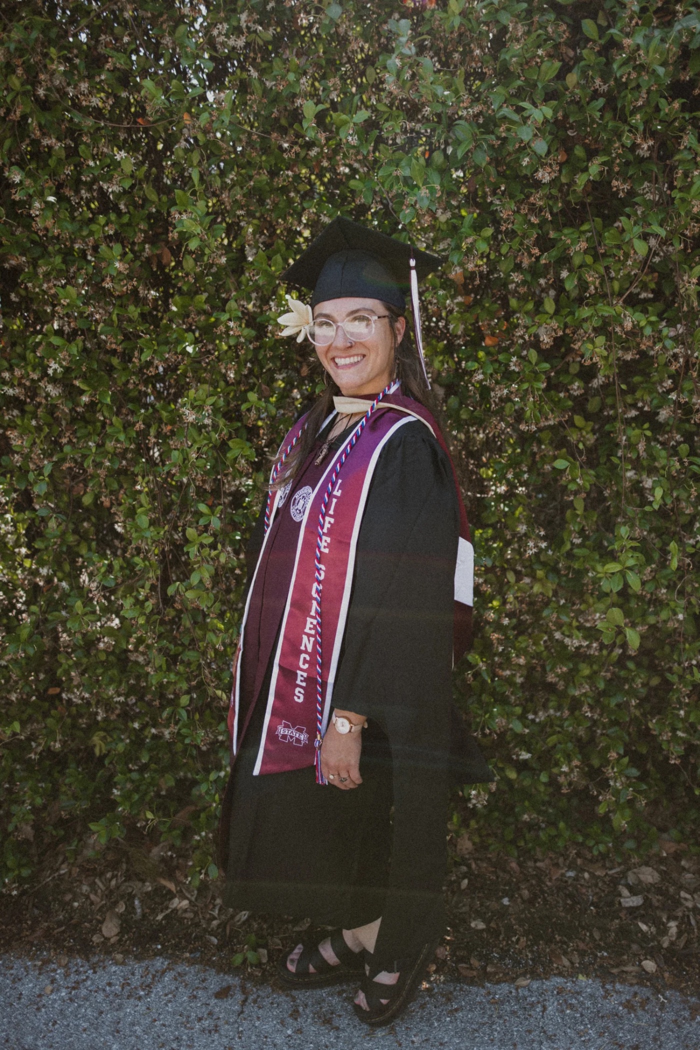 Madison Jenkins, founder of littleleaf, at her Mississippi State Life Sciences graduation against a wall of blooming jasmine